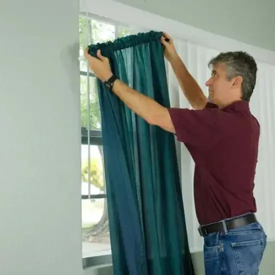 Installer hanging teal blackout curtains on a bedroom window rod for a home in Abu Dhabi.