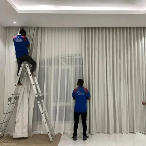 Professional installers fitting white wave curtains inside a modern Dubai home.