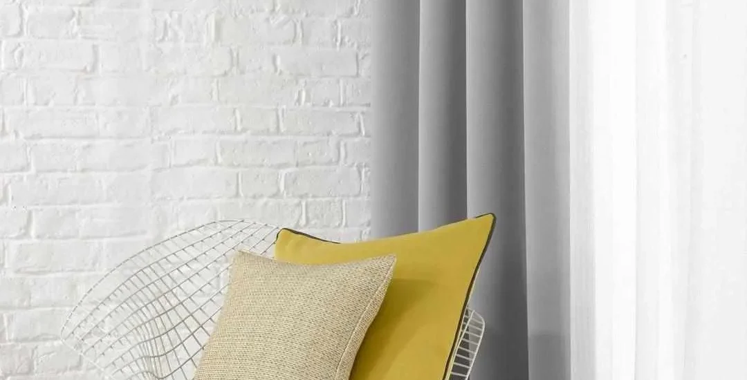 Grey and white curtains in a minimalist Dubai room with accent chair and brick wall.