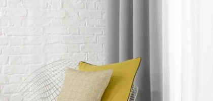 Grey and white curtains in a minimalist Dubai room with accent chair and brick wall.