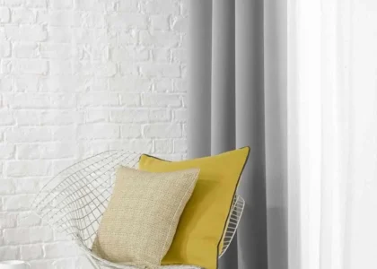 Grey and white curtains in a minimalist Dubai room with accent chair and brick wall.