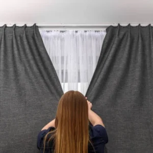 person opening layered fabric curtains revealing inner sheer curtain